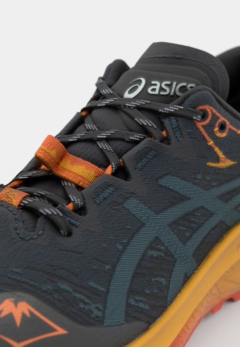 Baskets noires en tissu texturé, avec des accents orange et gris, des lacets texturés et une semelle en caoutchouc jaune-orange.