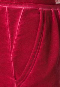 Sarkans audums ar gludu tekstūru, ar krokotu dizainu un sānu kabatām. Jostasvieta ir elastīga komforta un piemērotības nodrošināšanai.