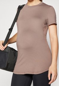 Brun kortärmad skjorta i mjukt tyg med rund halsringning, tillsammans med svarta leggings och en svart gymväska med ett nätackcent.