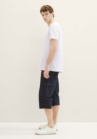Weißes Baumwoll-T-Shirt, knielange dunkelblaue Cargo-Shorts mit Taschen und weiße Sneaker. Einfaches Design, lockere Passform und glatte Textur.