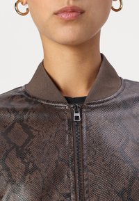Chaqueta bomber de piel sintética marrón con estampado de serpiente, que presenta un cierre de cremallera y cuello de canalé. Los detalles incluyen una cremallera oscura.