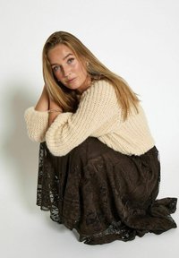 Chunky creme strikket sweater parret med en mørkebrun blondekjole. Outfittet har tekstureret stof og lagde designelementer.