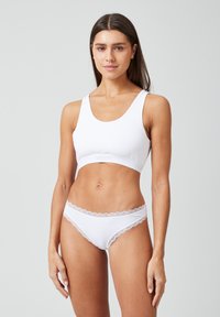Witte katoenen bralette met een ronde halslijn en brede bandjes, gecombineerd met witte slipjes met kantafwerking en een golvende rand.