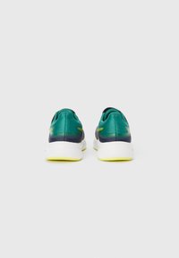 Des chaussures de course vertes et marine avec un dessus en maille texturée, présentant un intermédiaire blanc et des accents de semelle extérieure jaune vif.