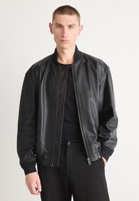 Zwarte leren bomberjack met een ritssluiting, geribbelde manchetten en een casual pasvorm. Zachte textuur en slank ontwerp met een minimalistische stijl.