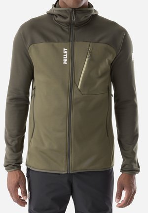 Man wearing olive green full-zip jacket with hood, zippered chest pocket, two side pockets, and white "Millet" logo on chest and sleeve.