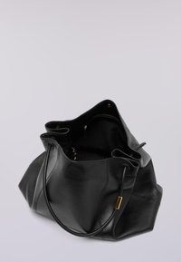 Svart läderväska med ett rymligt öppningsområde, mjuk textur, runda handtag och guldfärgade detaljer inuti. Har en minimalistisk design.