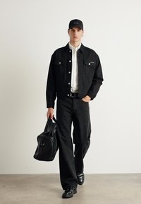 Musta farkkutakki nappikiinnityksellä, yhdistetty valkoisen paidan ja mustien leveiden farkkujen kanssa. Pitää mustaa urheilukassia, jalassa mustat lenkkarit.