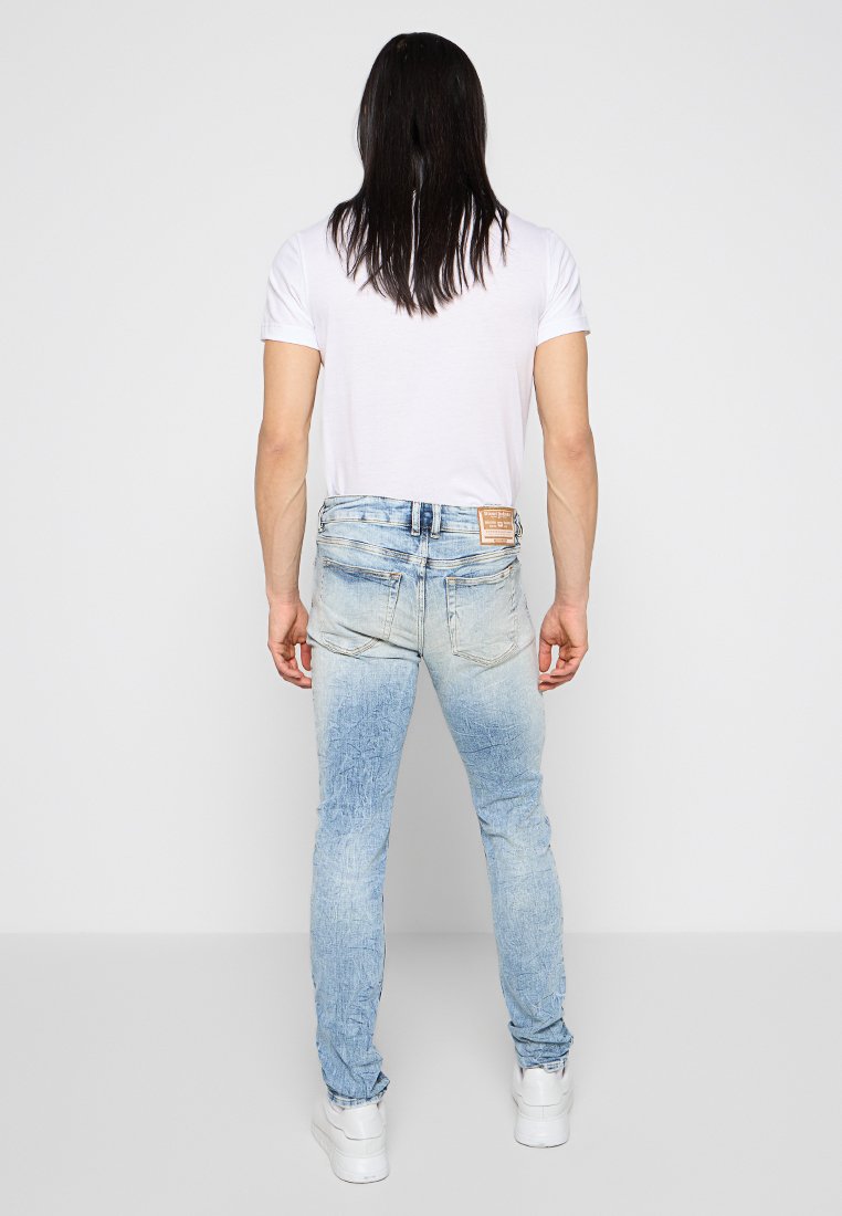 Jeans in denim azzurro chiaro con una texture scolorita, slim fit e una patch in pelle con il marchio sulla vita posteriore. Abbinati a una t-shirt bianca semplice.