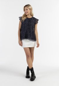 Blusa nera e multicolore con texture, maniche corte a balze, abbinata a una mini gonna bianca e stivali neri con lacci.