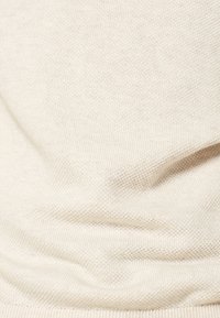 Tissu de pull beige clair tricoté avec un tissage texturé, doté d'un ourlet avec une bande lisse et extensible, offrant une apparence subtile et raffinée.