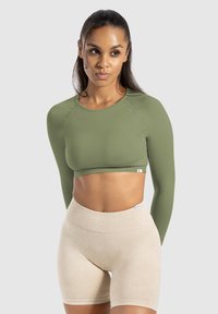 Lange mouwen crop top in olijfgroen, geribbelde textuur, ronde hals, aansluitende silhouet, gecombineerd met hoge beige shorts.