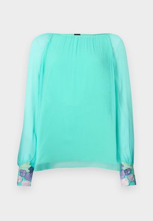 Mentolová blúzka s dlhými, nafúknutými rukávmi. Je zdobená vyšívanými kvetinovými akcentmi na manžetách. Vyrobená z ľahkej, priesvitnej látky.