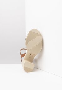 Scarpa con tacco alta beige con suola in gomma testurizzata, cinturini in pelle marrone e tacco a blocco. Il marchio "NeroGiardini" è visibile.