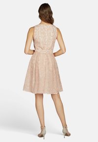 Ein ärmelloses, knielanges Kleid aus weichem rosa Spitzenstoff mit floralem Muster, das ein körperbetontes Oberteil und einen ausladenden Rock hat, der durch einen Taillengürtel betont wird.