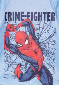 Blå t-skjorte med et grafisk motiv av en rød og blå Spider-Man i en actionpose, med teksten "KRIMINALITETSKJEMP" over og nettverksmønstre i bakgrunnen.