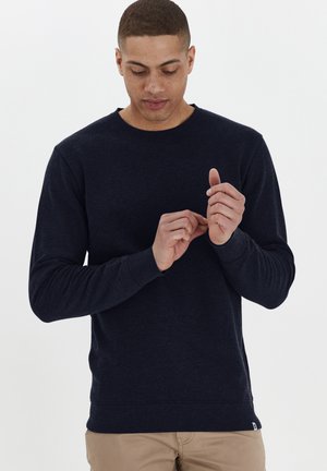 Marineblauwe sweatshirt met lange mouwen, gemaakt van zachte, gestructureerde stof. Heeft een ronde hals en ribgebreide manchetten. Draagt over lichtgekleurde broeken.