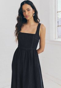 Robe en jean foncé avec un décolleté carré, des bretelles larges et une jupe froncée. Présente des coutures contrastées et une coupe décontractée.
