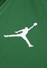 Tejido verde con una silueta blanca de una figura saltando con un balón de baloncesto. Superficie texturizada, diseño minimalista y contraste audaz.