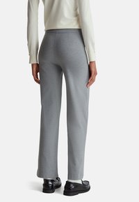 Szare długie spodnie w klasycznym kroju mają luźny krój, gładką teksturę oraz subtelny pionowy wzór. Noszone z czarnymi butami i kremowym swetrem.