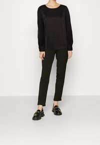 Svart, långärmad satinblus med rund halsringning, kombinerad med mörkgröna, slim-fit byxor och svarta platåloafers.