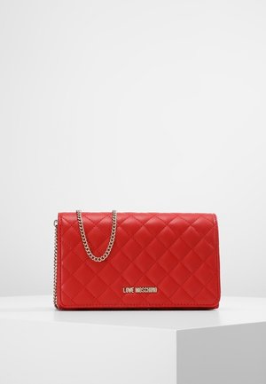 Sac bandoulière en cuir matelassé rouge avec une bandoulière chaîne dorée et un logo doré "Love Moschino" sur le devant, exposé sur un piédestal blanc.