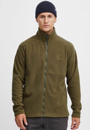Veste en polaire vert olive avec un col haut et une fermeture éclair intégrale. Dotée de manches raglan et d'un logo discret sur la poitrine. Texture douce.