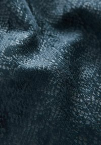 Texturerad tyg i djup teal med ett subtilt orm-skinnsmönster. Mjuk och sammetsliknande yta, med små variationer i ljusreflektion.