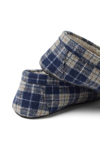 Zapatillas de tela a cuadros en azul marino y beige, con forro suave, puntera redonda y suela plana, que presentan una textura acogedora de lana y costuras cosidas.