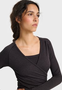 Schwarzes Wickel-Oberteil mit langen Ärmeln, gefertigt aus geripptem Stoff. Verfügt über einen tiefen V-Ausschnitt und ein Lagen-Design, das ein strukturiertes Muster an den Ärmeln zeigt.