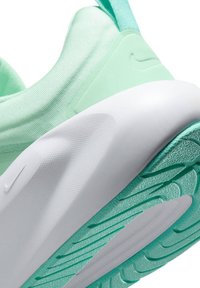 Gros plan sur le talon et la semelle d'une chaussure de sport vert menthe et blanche avec grip texturé et tige en tissu.