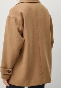 Bruine wolmix jas met een brede kraag, knoopsluiting bij de mouwen en een ontspannen pasvorm. Zachte textuur, middellange uitvoering, zichtbare stiksels op de rug.