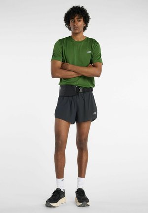 Grünes kurzärmeliges Sportshirt, schwarze Laufsport-Shorts mit integriertem Gürtel und schwarze Turnschuhe, kombiniert mit weißen Knöchelsocken.