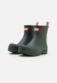 Green rubber ankle boots with a smooth finish, featuring red and white pull tabs at the back and a textured sole for grip.