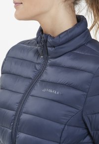 Mörkblå vadderad jacka med hög krage, med en framtida dragkedja och "WHISTLER"-logotypen i en kontrasterande färg på vänster sida.