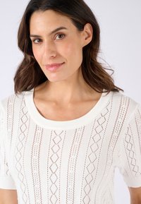 Witte gebreide top met een ronde hals, voorzien van een diamantpatroontextuur en korte mouwen. De stof lijkt lichtgewicht en ademend te zijn.