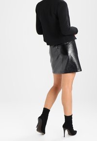 Černá kožená mini sukně s lesklým povrchem, doplněná o přiléhavý černý kabát a černé kotníkové boty na podpatku. Jednoduchý, čistý design.