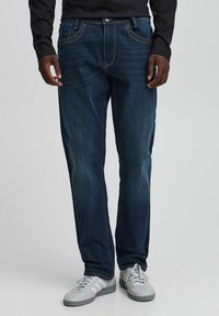 Mørkeblå jeans i denim med rette ben, kontraststing og fem lommer, brukt med grå joggesko.