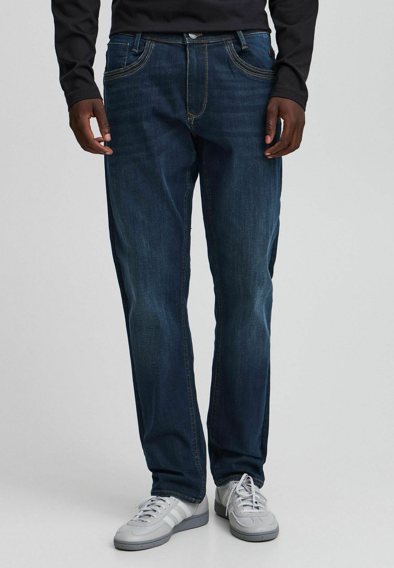 Mørkeblå jeans i denim med rette ben, kontraststing og fem lommer, brukt med grå joggesko.