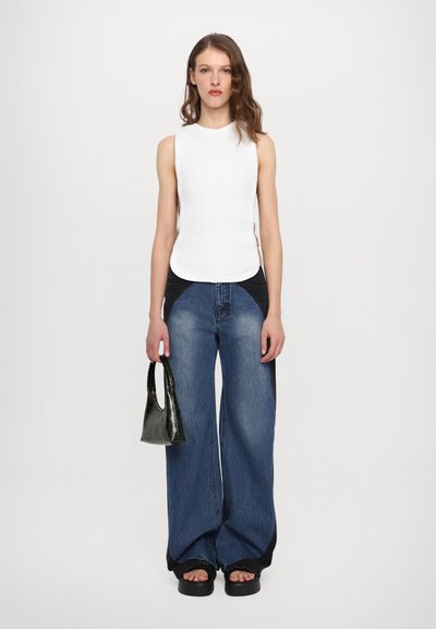 White sleeveless top, wide blue jeans with black accents, and a small black handbag with a crocodile texture. Platform sandals complete the look.