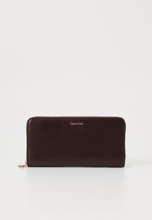 Calvin Klein wallet in dark burgundy leather, zippered closure, smooth texture, gold logo accent at the front, rectangular shape.