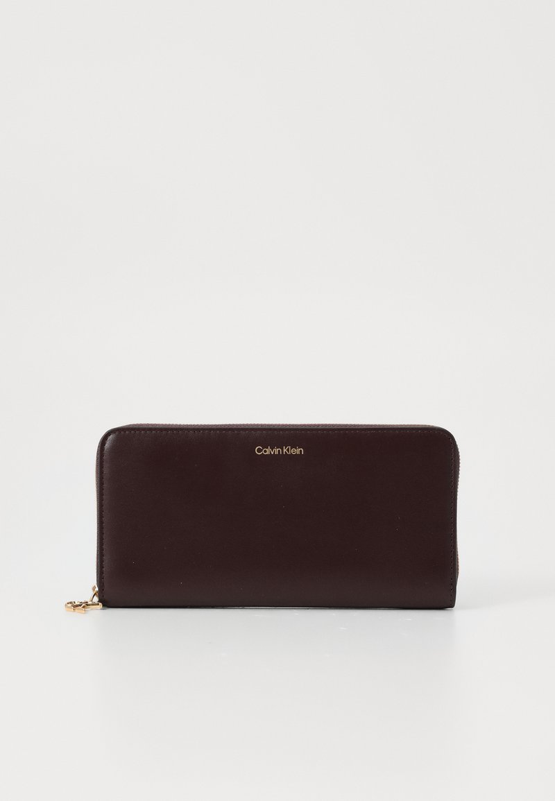 Calvin Klein novčanik u tamnom burgundcu, s patentnim zatvaračem, glatke teksture, zlatni logotip na prednjoj strani, pravokutnog oblika.