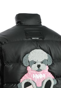 Chaquetón negro con collar redondeado y un perro gris texturizado bordado en la parte posterior, que lleva un suéter rosa.