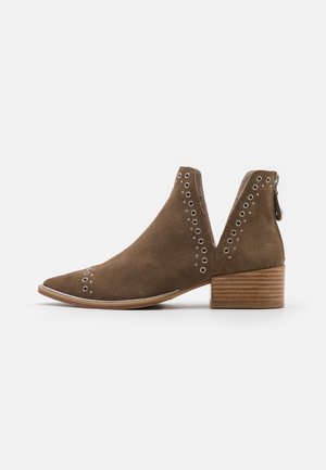 Bottine en daim marron avec talon bloc en bois empilé, œillets ronds en argent et fermeture éclair arrière sur fond blanc.
