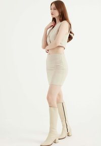 Top corto beige e gonna a vita alta con motivo a spina di pesce, abbinati a stivali beige al ginocchio con zip laterale.