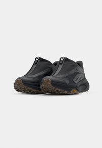 Des chaussures noires à enfiler présentent une tige texturée avec des zips, une semelle rembourrée et une semelle en caoutchouc à motifs pour une meilleure traction. Design léger.