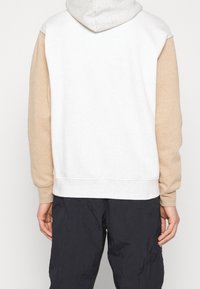 Felpa con cappuccio di colore grigio chiaro per il cappuccio, corpo bianco e maniche beige. Presenta polsini a coste e una vestibilità comoda.