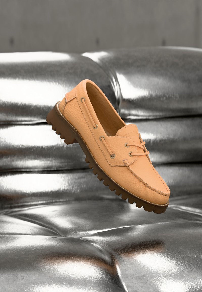 Mocassin en cuir marron clair avec une semelle robuste flottant au-dessus d'une surface argentée brillante et matelassée.