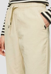 Beige corduroy broek met een elastische tailleband en een trekkoord. Voorzien van zijzakken en een textuurstof. Minimalistisch ontwerpaccenten.