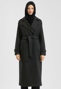 Lange zwarte wollen jas met een dubbelrijg ontwerp, brede revers, een riem in de taille en knoopmanchetten. Bevat een zwarte gebreide capuchon.